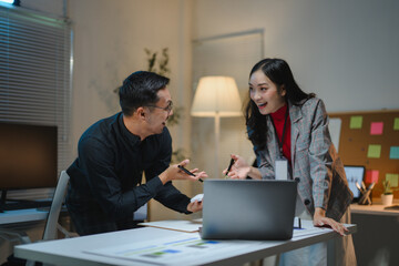 Obraz premium Asian businesspeople discussing and working late together using laptop in office at night