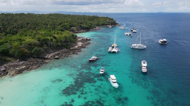 Aerial drone footage of Koh Racha Yai Island with many tour boats, yacht, catamaran and longtail boat anchoring around the bay. A popular destination for summer vacation activity in Phuket, Thailand.