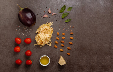 Flat lay of raw Italian pasta tagliatelle, fresh eggplant, cherry tomatoes, almonds, garlic, basil...