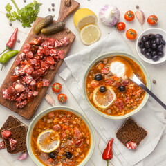 Traditional solyanka soup with smoked sausage, lemon slice, black olives, pickles, and rye bread...