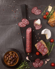 Top view of Italian salami sausage sliced on a black wooden serving board with creamy cheese...