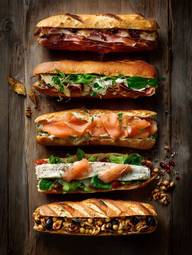 Delicious baguettes filled with various ingredients lying on wooden table