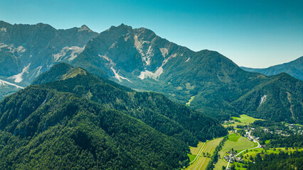 Aerial panoramic view of Zgornje Jezersko valley with lush green meadows, winding roads, and surrounding Kamnik-Savinja Alps under a clear summer sky in Slovenia. Scenic mountain landscape