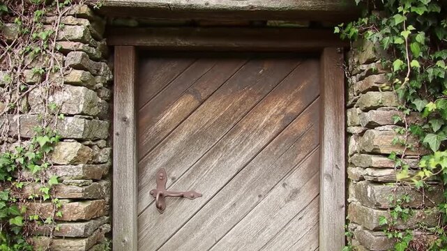 Medieval Wooden Door in Hillside Cottage &ndash; Rustic Stone-Framed Entrance Overgrown with Ivy, Historical Architecture