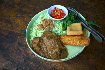 Green Basmati Rice, grilled chicken, fried tofu, fried tempeh, kenikir or cosmos caudatus leaves and sliced chili on a green plate on a wooden table