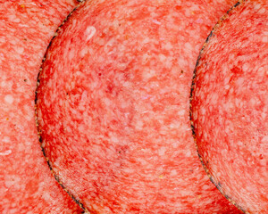 Close-up of thinly sliced italian salami overlapping in a textured pattern, vibrant pink and red cured meat on white background, appetizing food background for culinary projects.