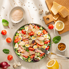 colorful spring salad with quail eggs, cherry tomatoes, radish slices, spinach leaves and parmesan shards on marble background, fresh healthy lunch, bright daylight, uplifting wellness concept