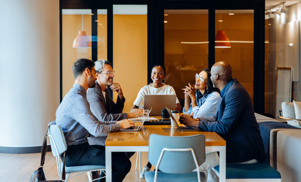 Group discussing strategies in an office with laptops and cheerful interaction - Powered by Adobe