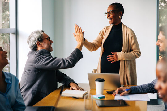 Pregnant woman high-fiving colleague in a casual business meeting