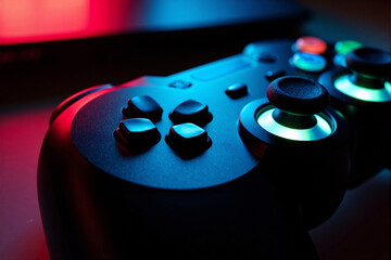 Close-up of a black video game controller illuminated by dramatic red and blue neon lights, focusing on the analog sticks for an intense gaming and esports concept
