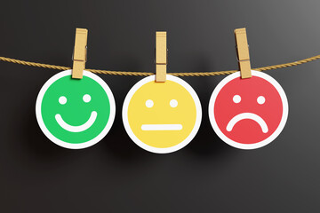 Circular green smile emoji, yellow sternness icon and red sadness symbol being hung by clothes pegs on a thin rope on a black background. Illustration of the concept of emotions and facial expressions