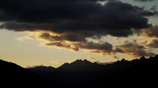 Dramatic mountain sunset with moving clouds and silhouetted peaks