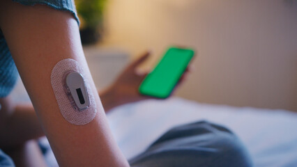 Close Up Of Diabetic Girl Sitting On Bed At Home Checking Insulin Levels On Mobile Phone App