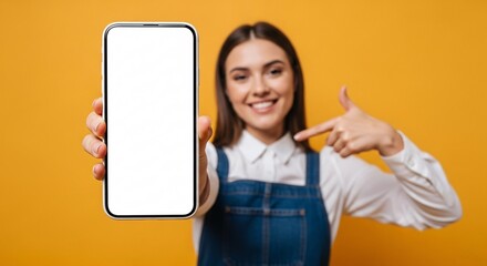 Smiling young woman pointing to blank smartphone screen – mockup space for app, website, or marketing design