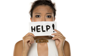 Studio shot on white background showing anxious Asian woman holding paper with word HELP in front of mouth.
