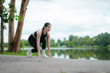 Young sportswoman preparing for running near lake in city park