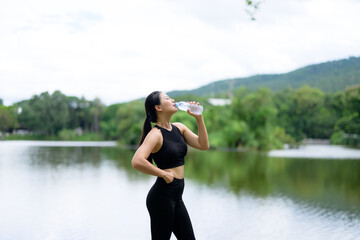 Sporty woman drinking water from bottle after exercising in park near lake