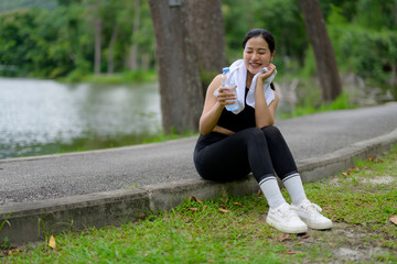 Young sportswoman resting and drinking water in a park by the lake