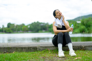 Asian sportswoman resting after training by the lake wiping sweat with towel