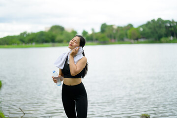 Young sportswoman wiping sweat with towel after training near lake