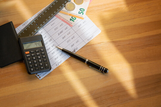 Euro banknotes next to a sheet with financial calculations, calculator and black pen on wooden table in bright sunlight, money and household budget, investments and savings, utility bill calculation. - Powered by Adobe