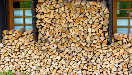 Neatly stacked firewood logs pile near traditional wooden house with green windows during summer....