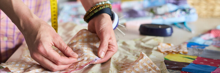 Caucasian woman hands arranging fabric pieces on table, preparing for sewing project, wearing...