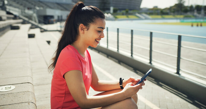 Athlete, woman and relax with phone at stadium for social media, fitness app and event agenda. Female person, resting and mobile for texting, sports progress results and information for tournament - Powered by Adobe