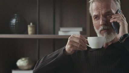 Tilt up medium close up shot of Caucasian mid-adult businessman drinking cup of hot coffee while calling on mobile phone at office desk - Powered by Adobe