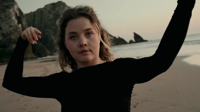 A woman elegantly dances on a serene beach at sunset, capturing a tranquil and expressive moment by the ocean.