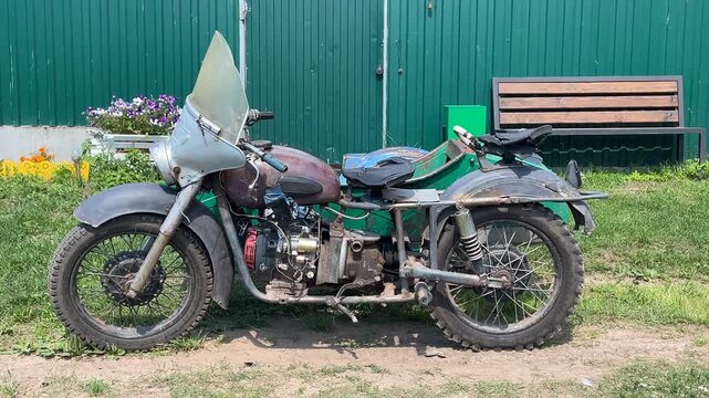 Vintage motorcycle with sidecar parked outdoors on grass near a wooden bench and green wall