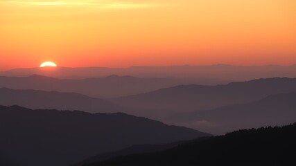 Fototapeta premium Orange Sunset over Silhouetted Mountain Ranges Layers of hazy purple and dark silhouettes at dusk mountains