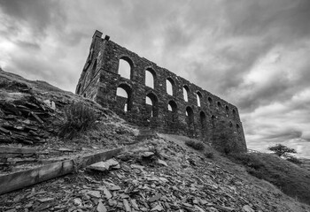 Monochrome view of the tall stone wall with multiple arched openings at Cwmorthin Slate Mill, set...