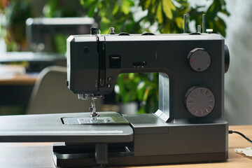 Modern sewing machine standing on table in workspace, metallic body featuring adjustment dials and...