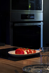 Spotlight on a plate of tomatoes with mozzarella cheese in a dimly lit kitchen