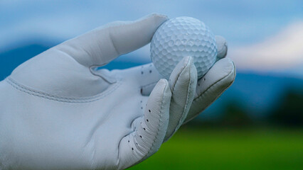 Hand-wearing golf glove holding a white golf ball on green background.