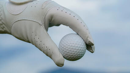 Hand-wearing golf glove holding a white golf ball on green background.