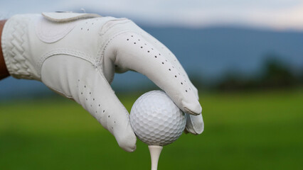 Hand-wearing golf glove holding a white golf ball on green background.