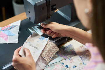 Young adult Caucasian woman sewing fabric pieces with sewing machine, hands adjusting textile while...