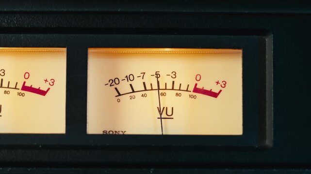 Analog dial indicator of audio signal level amplifier. Vintage arrow moves with sound level. Round classic volume indicator with yellow backlight, VU meters. Close-up of old measuring dB decibels