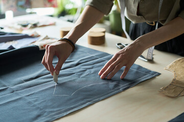 Caucasian young adult woman marking fabric with tailors chalk on worktable, hands drawing pattern...