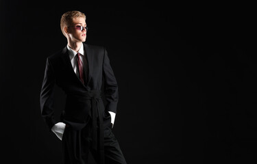Obraz premium Handsome young man wearing stylish suit and sunglasses on black background, space for text