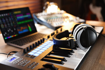 MIDI keyboard with headphones, laptop and dj mixer on wooden table indoors, closeup