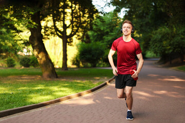 Smiling sportsman in headphones running with bottle outdoors. Morning exercise