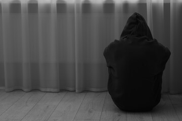Sadness and depression. Silhouette of man in hoodie near curtains at home, back view and space for...