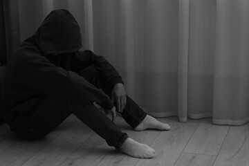 Sadness and depression. Man in hoodie near curtains at home. Black and white effect