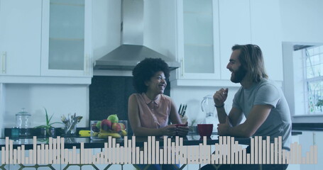 Talking couple holding red mugs and smiling at home kitchen island, with fruit bowl, utensil holder