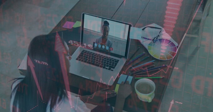 Taking notes during virtual meeting at wooden desk, with laptop, color wheel, financial graphs - Powered by Adobe