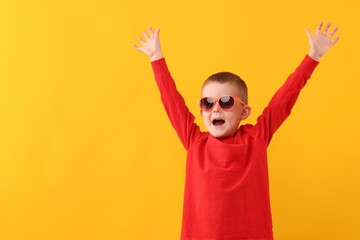 Cute little boy in sunglasses laughing on yellow background