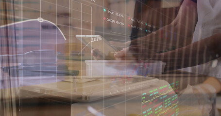 Worker analyzing tablet above white box at worktable, with shelves, financial charts overlay
